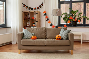 holidays, decoration and party concept - home room with jack-o-lanterns or pumpkins on sofa and...