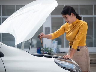 Asian woman is checking oil level in car engine.