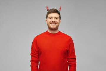 holiday, theme party and people concept - happy smiling man in halloween costume of devil over grey...