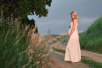 Fototapeta na wymiar Pregnant young woman in white dress on posing in summer natural park