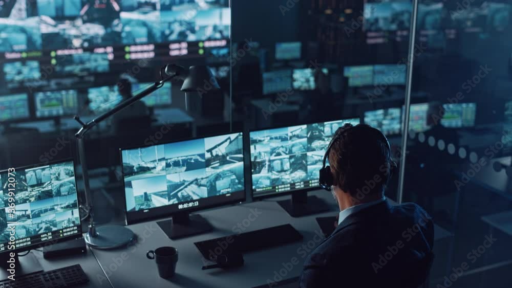 Poster Male Officer Works on a Computer with Surveillance CCTV Video Footage in a Harbour Monitoring Center with Multiple Cameras on a Big Digital Screen. Employees Sit in Front of Displays with Big Data.