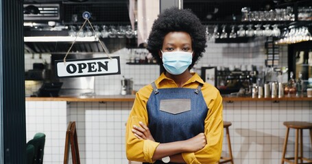 Portrait of beautiful African American young woman waitress in apron and medical looking to camera...