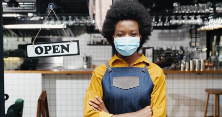 Portrait of beautiful African American young woman waitress in apron and medical looking to camera...