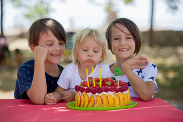 Sweet little blond toddler boy, celebrating his third birthday in a park with siblings and friends