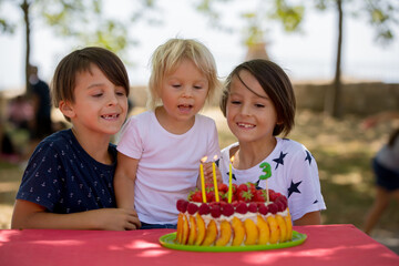 Sweet little blond toddler boy, celebrating his third birthday in a park with siblings and friends