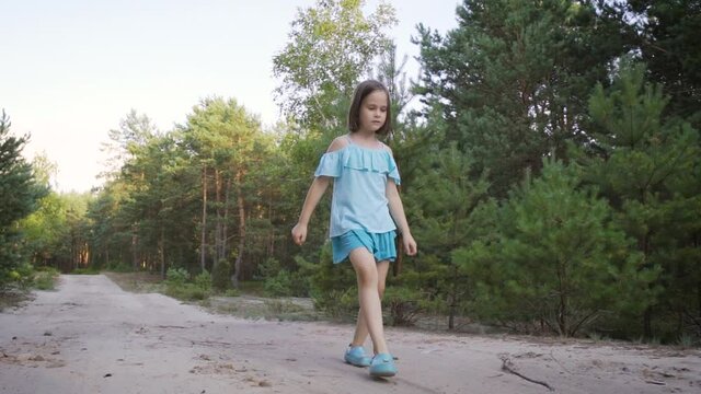cute girl walks backwards on a forest road in summer