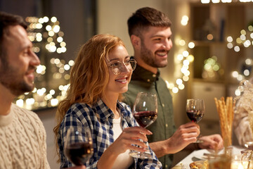 holidays, celebration and people concept - happy friends having christmas dinner at home drinking red wine