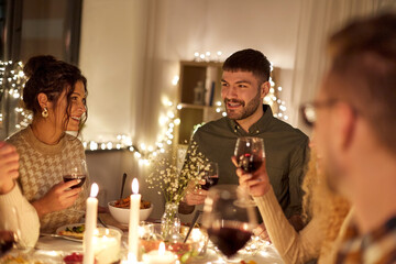 holidays, celebration and people concept - happy friends having christmas dinner party and drinking non-alcoholic red wine at home