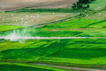 Vehicle driving on unpaved road making dust through the wonderful and beautiful rural scenic landscape,Avena Sativa,Oat green field.