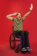 Scared, shocked. Caucasian young disabled man's portrait on red studio background. Beautiful male model in casual style. Concept of human emotions, facial expression, sales, ad, inclusion. Copyspace.