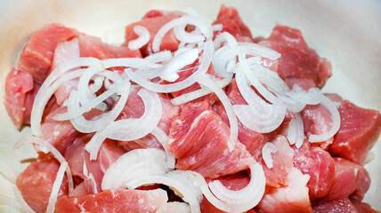 Raw meat cut into chunks with onion half-rings. Harvesting meat for a picnic.