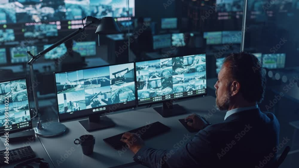 Poster Male Officer Works on a Computer with Surveillance CCTV Video Footage in a Harbour Monitoring Center with Multiple Cameras on a Big Digital Screen. Employees Sit in Front of Displays with Big Data.