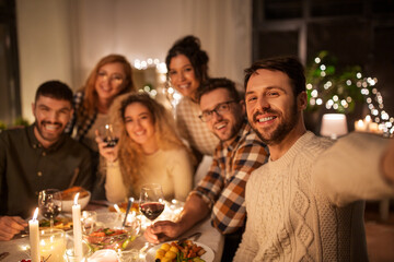 holidays, celebration and people concept - happy friends taking selfie at home christmas dinner party
