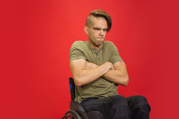 Offended. Caucasian young disabled man's portrait isolated on red studio background. Beautiful male model in casual style. Concept of human emotions, facial expression, sales, ad, inclusion. Copyspace