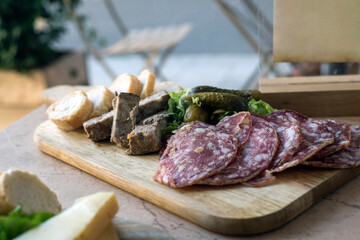 Closeup of slices of saussage and bread on a wooden cutting board on the table at the restaurant terrace