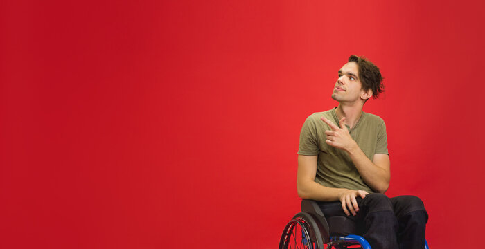 Pointing, Flyer. Caucasian Young Disabled Man's Portrait Isolated On Red Studio Background. Beautiful Male Model In Casual. Concept Of Human Emotions, Facial Expression, Sales, Ad, Inclusion