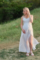 Fototapeta na wymiar Pregnant woman in white dress posing in the park