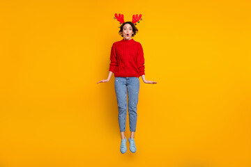 Full length photo of pretty lady jump high up unexpected surprise party open mouth shocked wear decor headband x-mas horns red knitted sweater jeans shoes isolated yellow color background