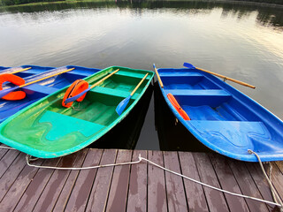 blue and green boats with oars and orange lifebuoys are moored to a wooden pier on the lake in the...