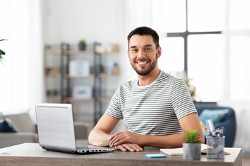 technology, remote job and business concept - happy smiling man with laptop computer working at...