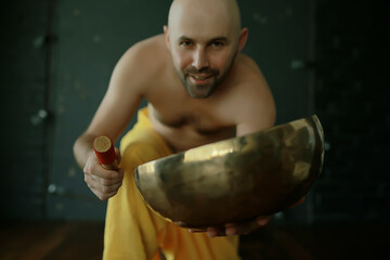 Tibetan singing bowl, a monk in yellow pants meditates and plays the musical bowl, Buddhism, religion