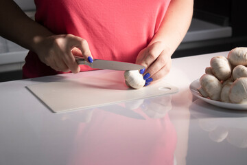 girl's hands cut champignon mushrooms on a white plastic board on a white table top. cooking process. High quality photo