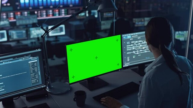 Female Software Engineer Working in a Modern Monitoring Office with Green Screen Mock Up on a Computer Display. Monitoring Room Big Data Scientists and Managers Sit in Front of Computers.