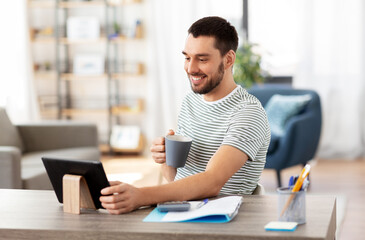technology, remote job and lifestyle concept - happy smiling man with tablet pc computer drinking coffee or tea at home office
