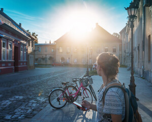 Young woman with a smartphone in her hands on the street in a European city, vintage building and parked bicycles. Bicycle rental in the city
