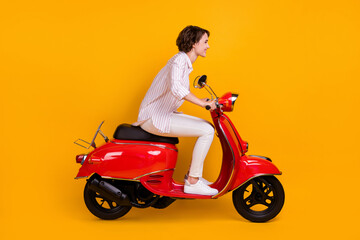 Fototapeta na wymiar Side profile full length photo of lovely funny young girl riding scooter enjoying country road high speed lover wear white striped shirt pants isolated yellow vivid color background