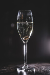 Two wedding gold rings fall into a glass of champagne against black background. Brides and groom wedding rings. 