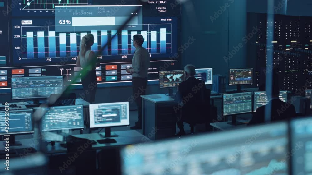 Aufkleber Two Software Engineers Talking Next to a Big Screen in a Modern Monitoring Office with Live Analysis Feed with Charts. Monitoring Room Big Data Scientists and Managers Sit in Front of Computers.