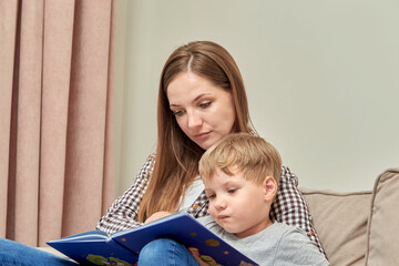 A young mother teaches her preschool son to read. Open book.