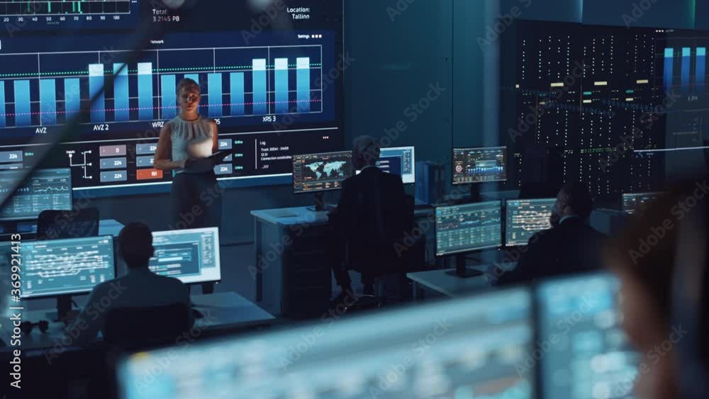 Fototapete Female Software Engineer Making a Presentation in a Modern Monitoring Office with Live Analysis with Charts on a Big Screen. Monitoring Room Big Data Scientists and Managers Sit in Front of Computers.