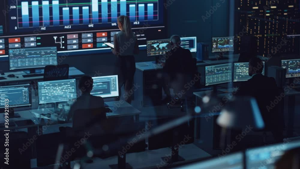 Poster Software Engineers Working in a Room with a Big Screen in a Modern Monitoring Office with Live Analysis Feed with Charts. Monitoring Room Big Data Scientists and Managers Sit in Front of Computers.