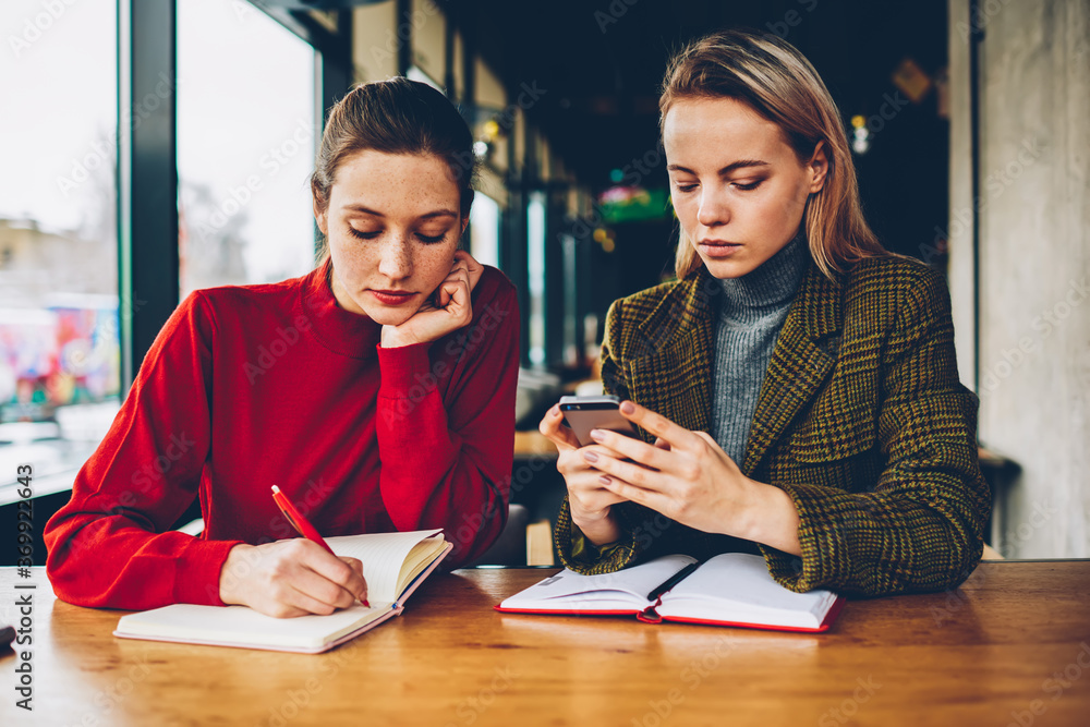 Poster skilled student writing down test in notepad while female tutor reading notification on smartphone d