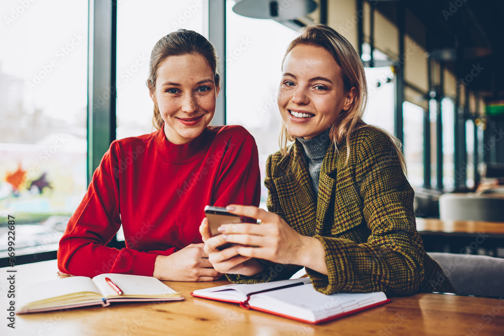 Poster portrait of two happy bloggers smiling at camera while discussing new funny application installed on