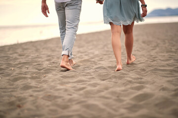 cropped image of  young couple in casual barefoot walk on sandy beach