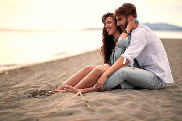 young beautiful couple sitting on the sandy beach, enjoying, smiling, hugging