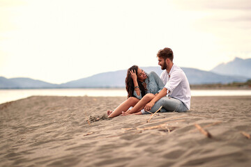 young beautiful couple sitting on the sandy beach, enjoying, smiling, looking each other