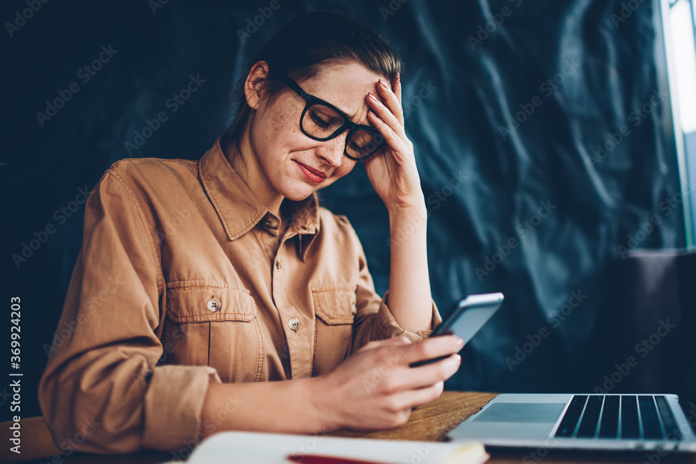 Poster worried hipster blogger crying while reading incoming sms message with bad news on smartphone device