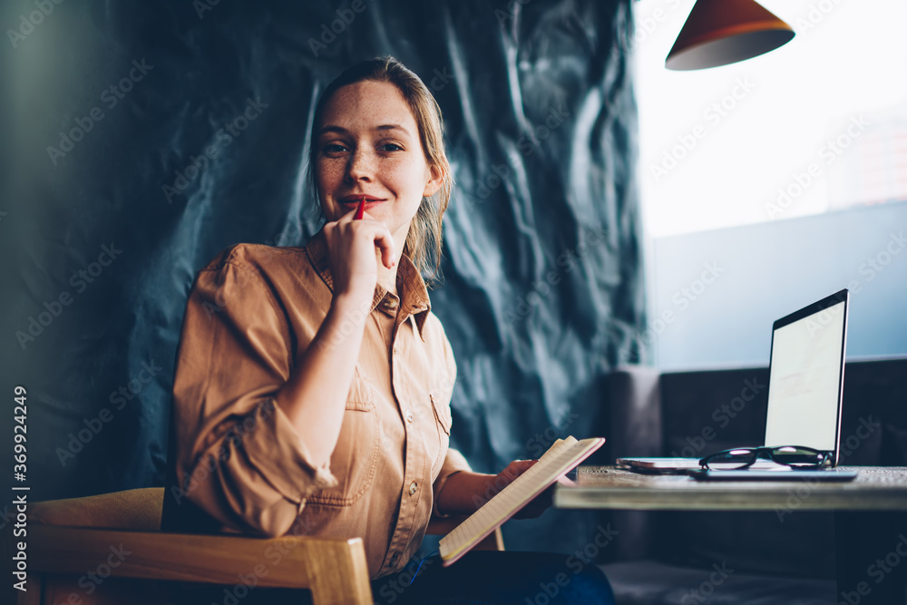 Aufkleber portrait of pretty talented hipster girl with pen in hand looking at camera while sitting with noteb