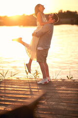  beardy guy hugging, lifting up his girlfriend at sunset by the river