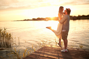 Fototapeta premium beardy guy holding up his girlfriend at sunset by the river