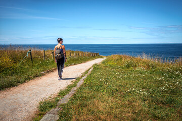 Una chica recorre un sendero que discurre junto al Mar Cantábrico.