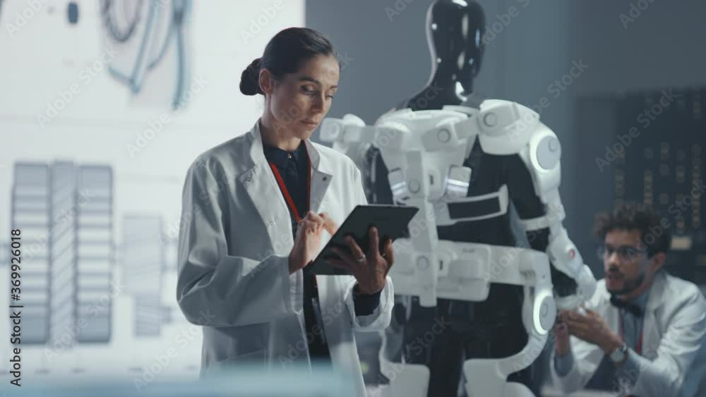 Poster In Development Laboratory: Portrait of a Beautiful Chief Female Engineer Using Digital Tablet Computer. Scientists Work on Prototype Exoskeleton Designed to Help Disabled People, Hard Labor Workers