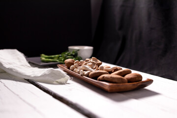 variety of mushrooms on wooden plate and broccoli on black plate for cooking in vegan food