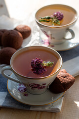 delicious tea with clover in a beautiful white set with pink flowers and a saucer with brown cookies