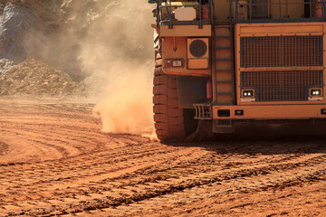 Large mining dump truck lifts orange dust on wheels  © MaksimM