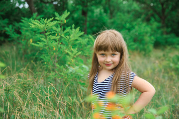 Naklejka na ściany i meble Portrait of a little girl on a natural green background. The background is blurred.
